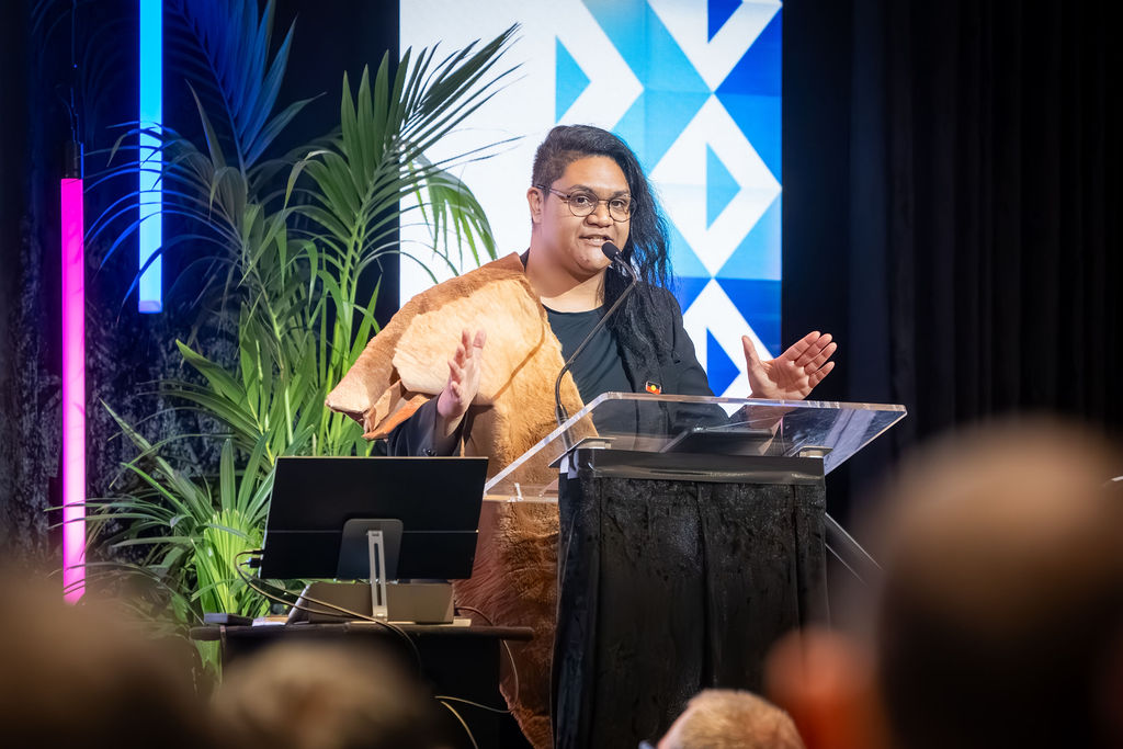 A keynote speaker addressing delegates from a lit conference stage